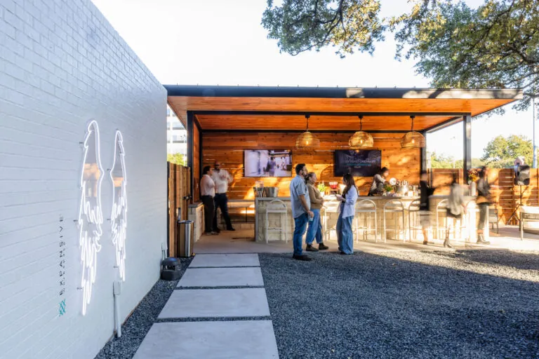 Expansive Austin Highland outdoor covered patio and bar area with neon angel wings mural on white brick wall