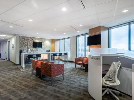 Regus Downtown Superdome high-rise lounge with patterned carpet, red-orange armchairs, ThinkPod workstation, and city views