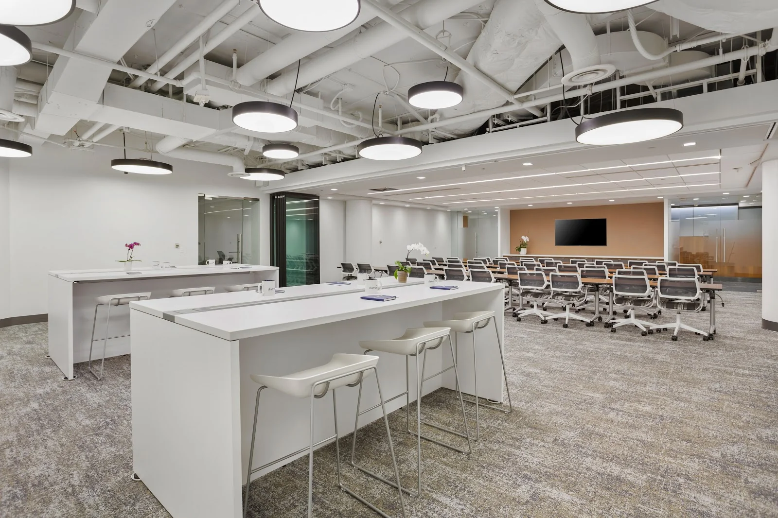 District Offices Pennsylvania Avenue white modern event space with round pendant lights, bar tables, and peach accent wall