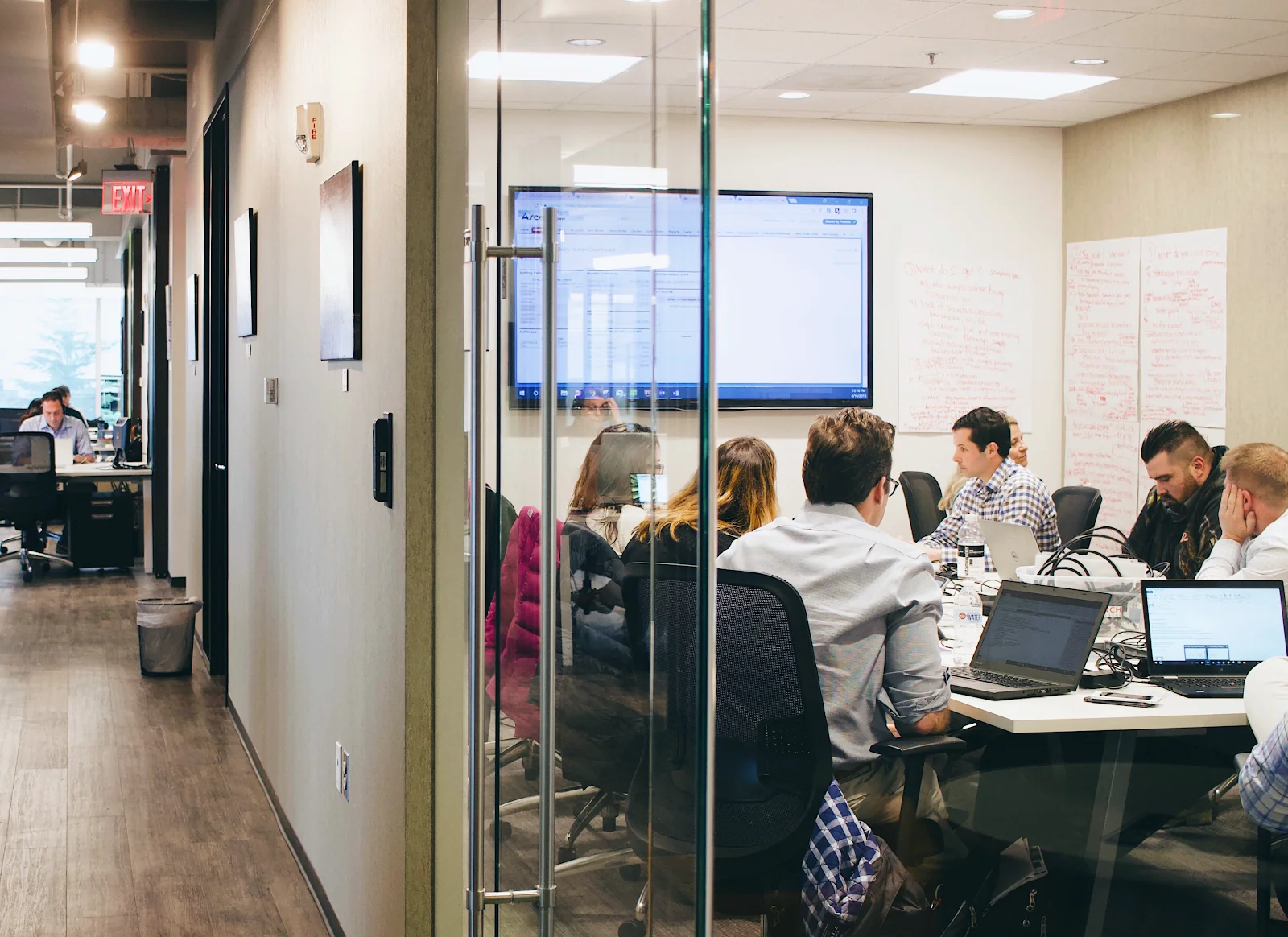 Launch Workplaces team meeting in glass-walled conference room with whiteboard notes, TV screen, and professionals working on laptops