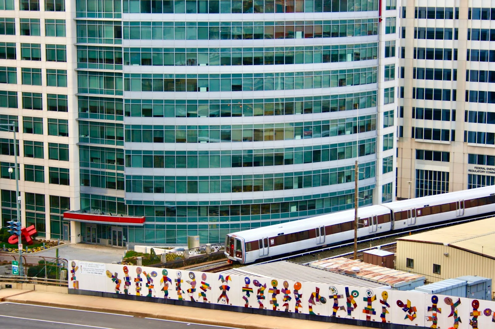 Noma Workspaces glass curtain-wall office building exterior with DC Metro train passing and colorful street mural